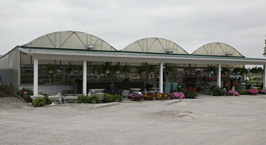 Large three domed greenhouse with various concrete statues and bird baths, hanging plants at entrance.