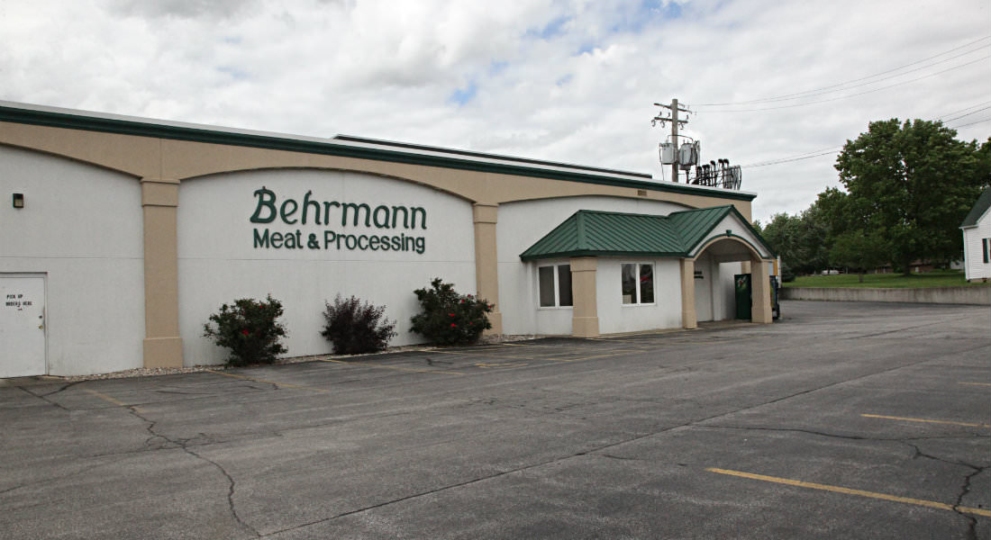 Tan and cream building with green room, Behrmann Meat and Processing Sign, three bushes with berries.