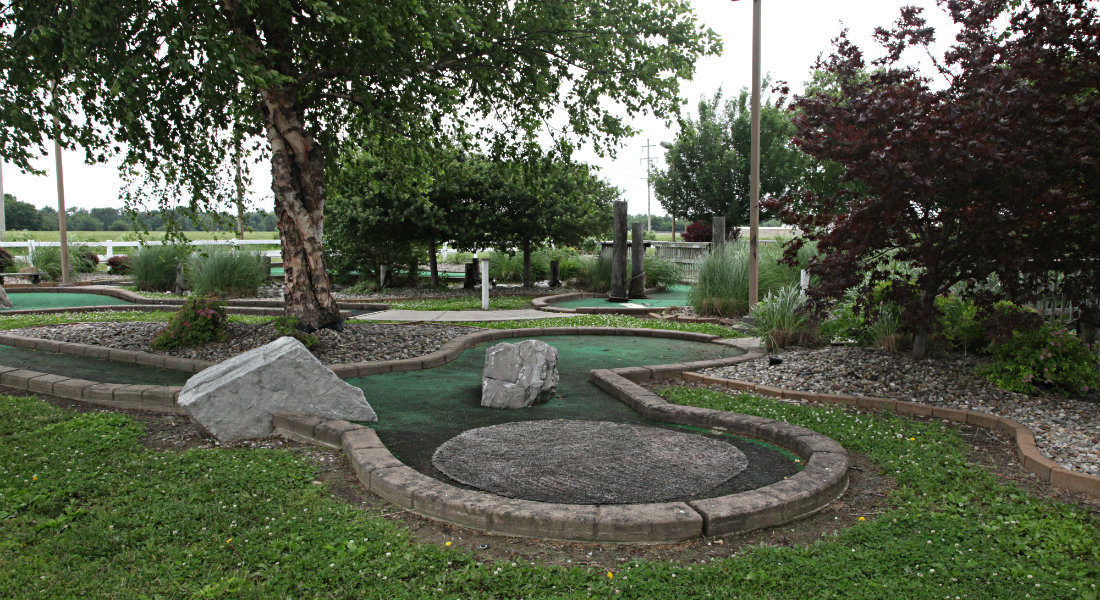 Miniature golf course putting greens with trees and grass surounding.