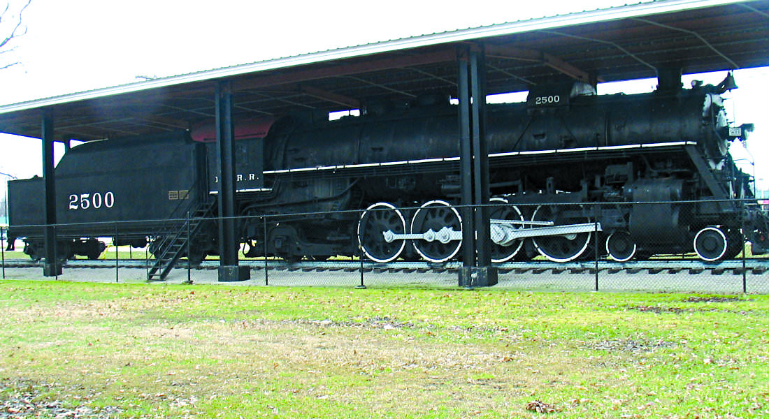 Black train cars sitting under covered depot with stairs to get into cars and number 2500 on side. 