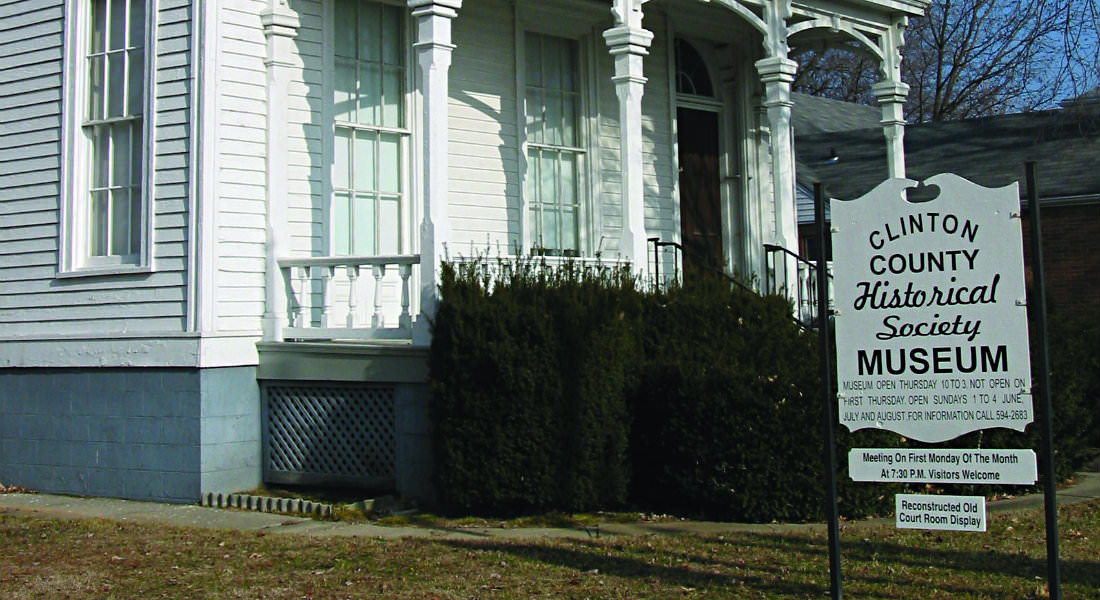 Large white victorian house with blue foundation, rectangular sign with text: Clinton County Historical Society Museum.