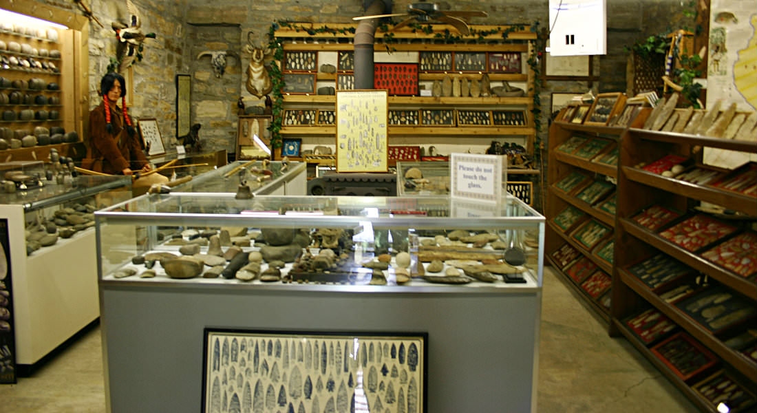 Room with glass display cases and shelving on both sides with Indian artifacts, Indian Statue with braids.