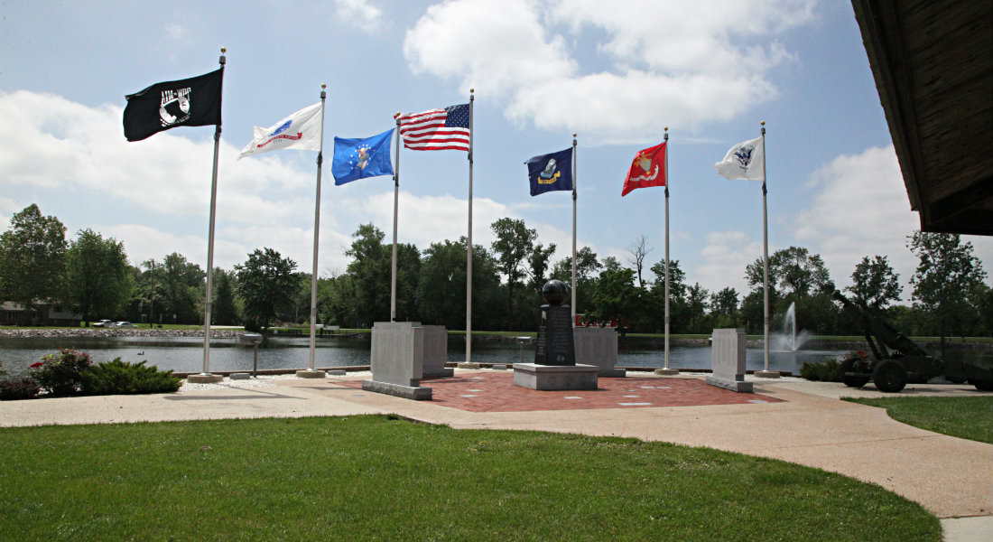 Cement Memorial Walls with engraved names by stream, Amerian Flag and 6 others on poles around memroial., water fountain.