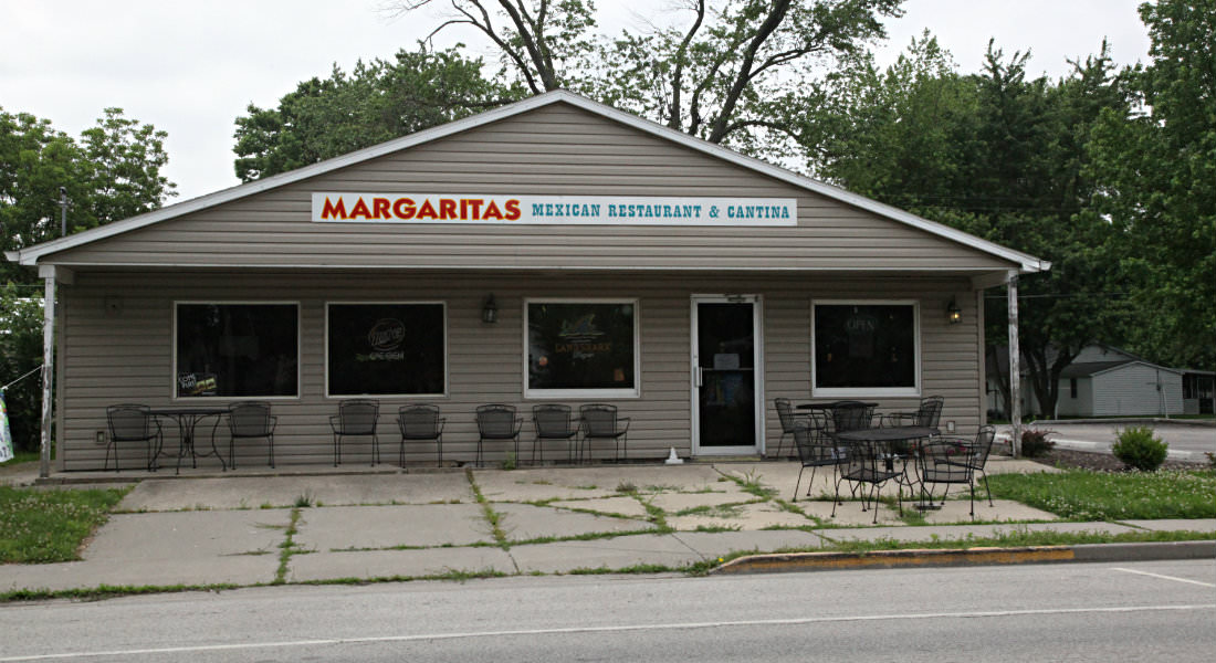 Tan sided building with covered porch with metal tables and chairs, sign for Margaritas Mexican Restaurant and Cantina.