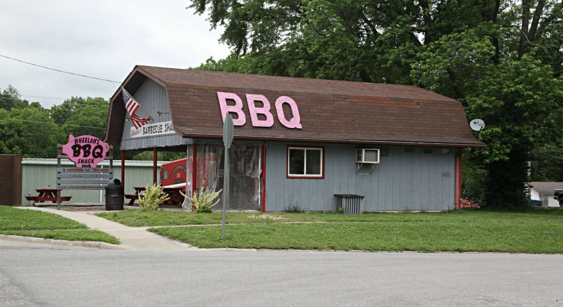 Grey building with brown roof that looks like barn, Pink pig shaped Sign Wheelan's BBQ Shack