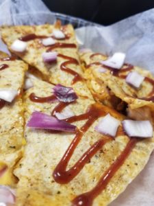 A chicken quesadilla drizzled with BBQ sauce and sprinkled with chopped red onions.