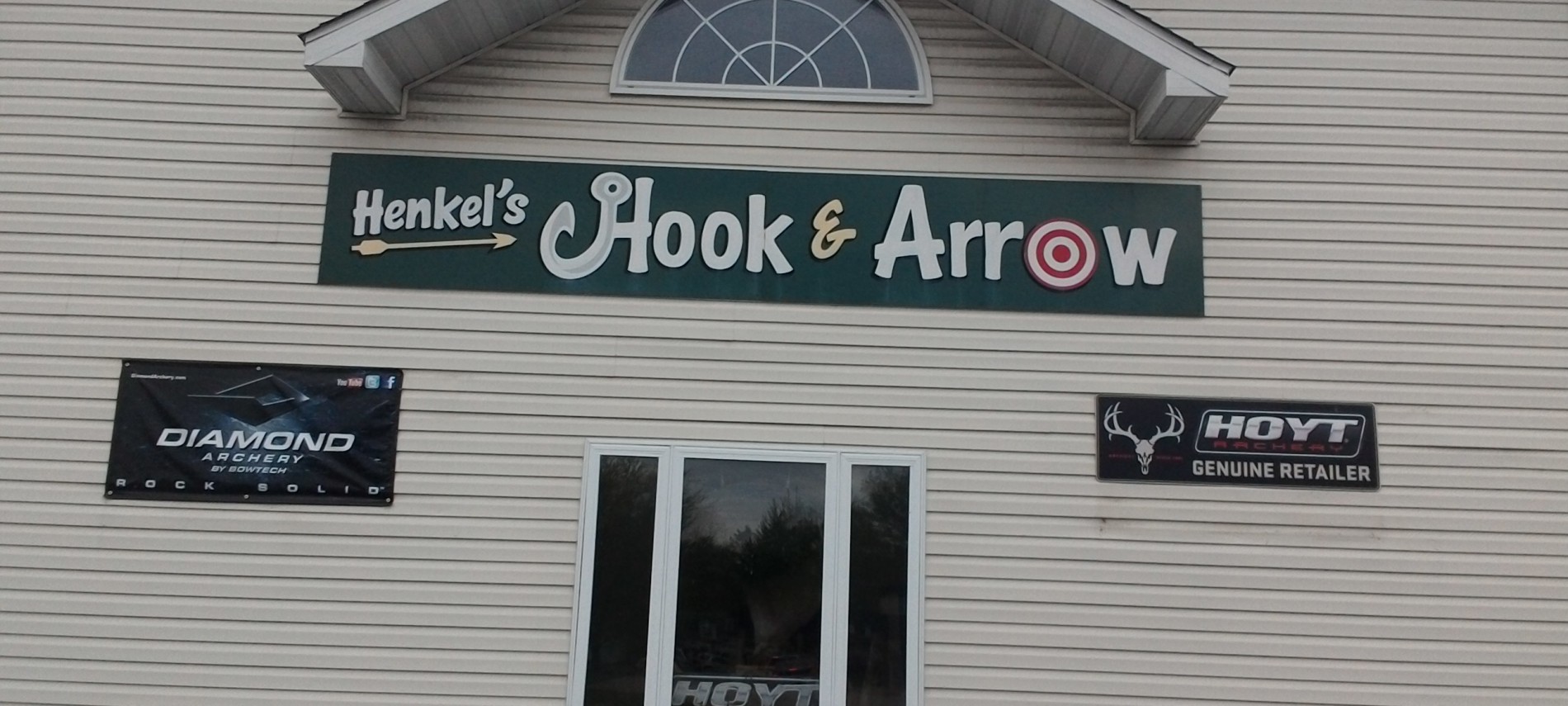Tan sided multi-story building with Black Sign: Henkel's Hook & Arrow, sign for Diamond Archery and Hoyt Retailer.