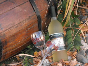 A white wine bottle and glass leaning against an old wooden trunk.