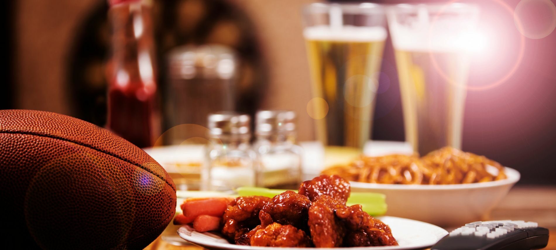 Plate of wings next to a football, with onion rings, and two beers