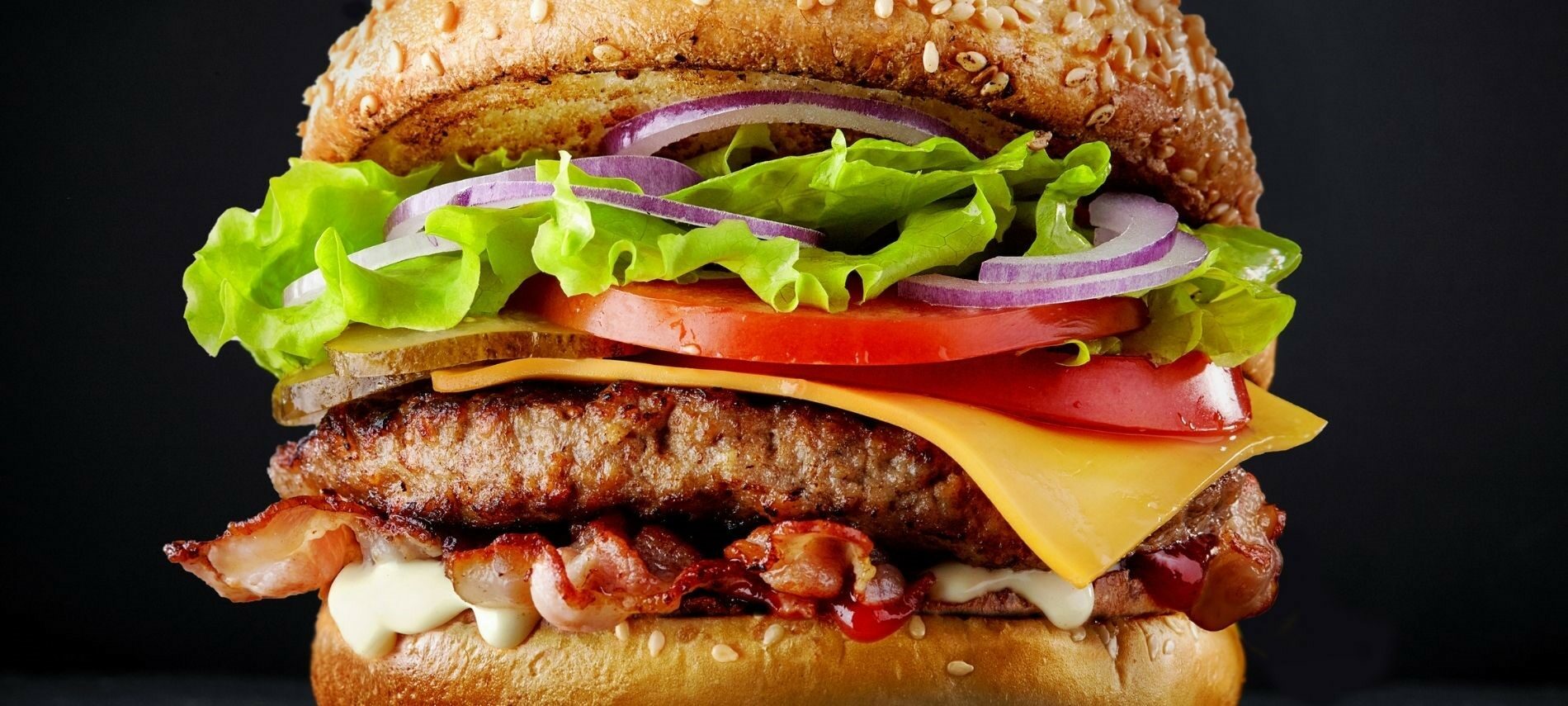 Closeup of a loaded burger—cheese, bacon, burger, tomato, lettuce, onion on a toasted bun