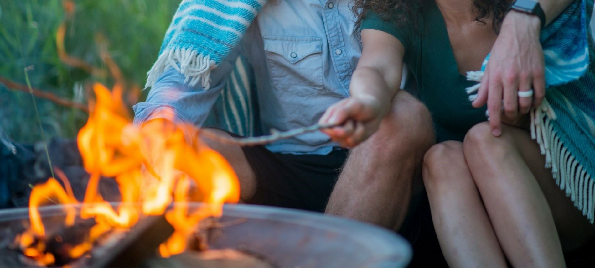 Couple sitting by outdoor firepit roasting marshmallows