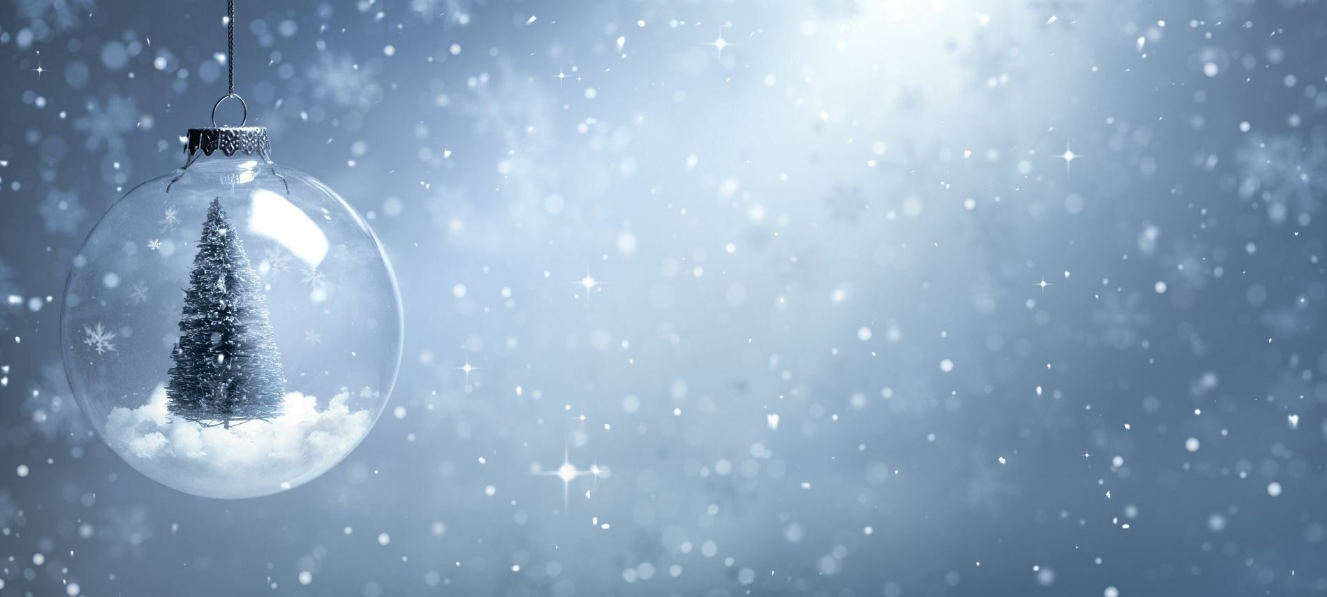Single clear bulb with a Christmas tree inside surrounded by sparkling snow flurries against a gray background