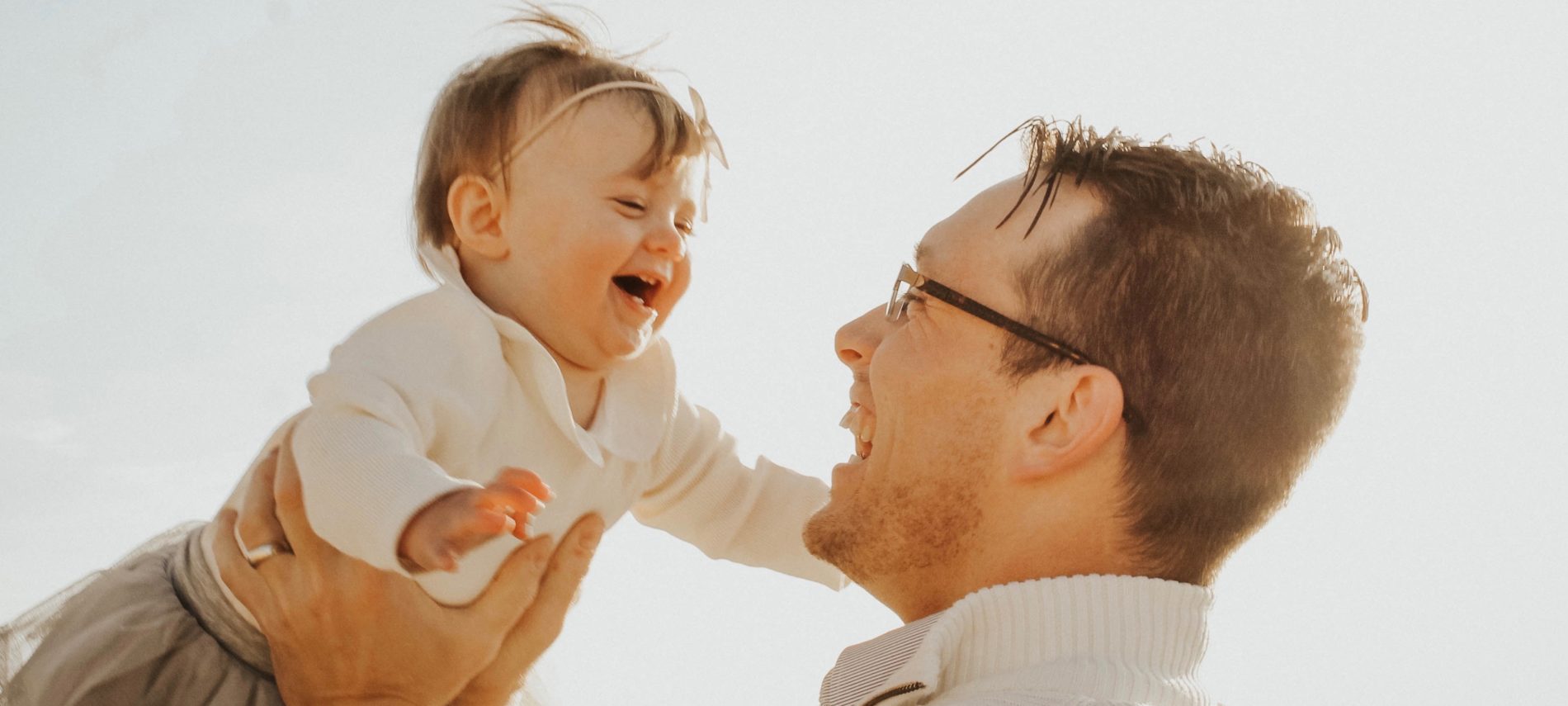 Dad raising little daughter over his head as she laughs with delight.