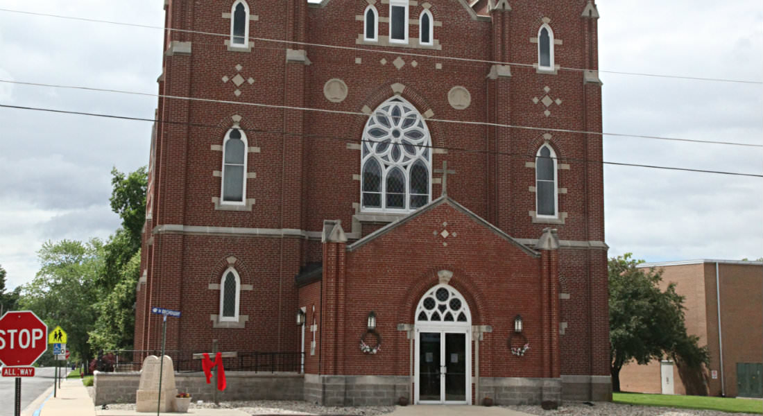 Three story red brick church on corner, Stop and children crossing sign, cross with red draped material.